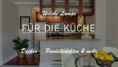 Ausschnitt einer kleinen offenen Küche mit Übergang in das Wohnzimmer. Die Küche ist durch eine Theke abgetrennt. Dahinter erkennt man eine Beleuchtung durch zwei Wandbeleuchtungen. Das Bild ist leicht abgedunkelt, sodass man den Titel leichter erkennen kann: "Welche Lampe für die Küche?"